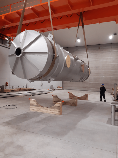 Overhead gantry crane lifting a large-scale stainless steel industrial scrubber during the assembly process in the workshop