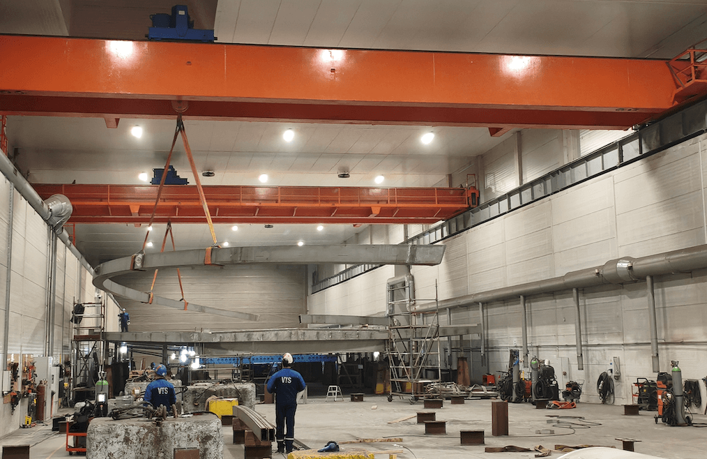 Two 30‑ton gantry cranes lifting a duplex steel bridge arch inside a workshop