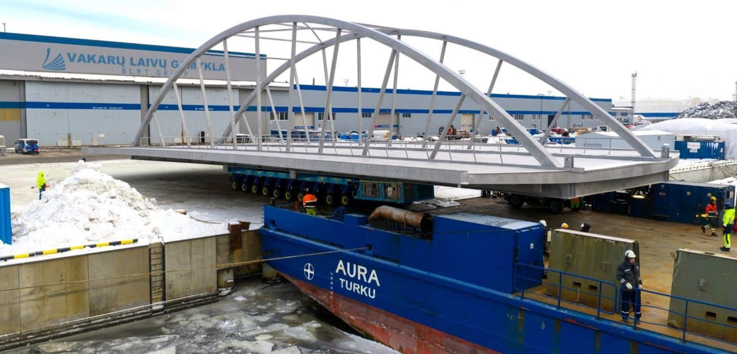 Härnön duplex stainless steel bridge for Härnösand being transported from the sea‑pier assembly area using SPMTs for Ro‑Ro loading onto a cargo vessel after fabrication by Western Technological Solutions, prior to sea delivery to Härnösand