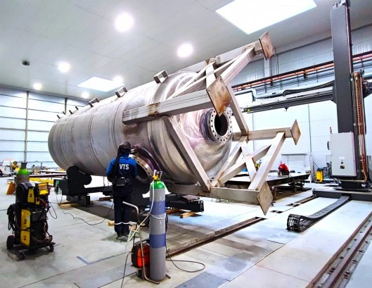 Welder welding a large stainless-steel pressure vessel during assembly inside a modern fabrication workshop with advanced equipment in Klaipeda