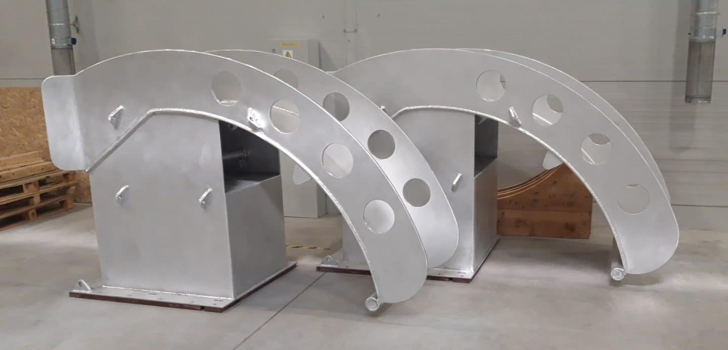 Two large welded aluminum saddle supports with perforated curved arms, manufactured for heavy duty LNG marine applications inside an industrial workshop