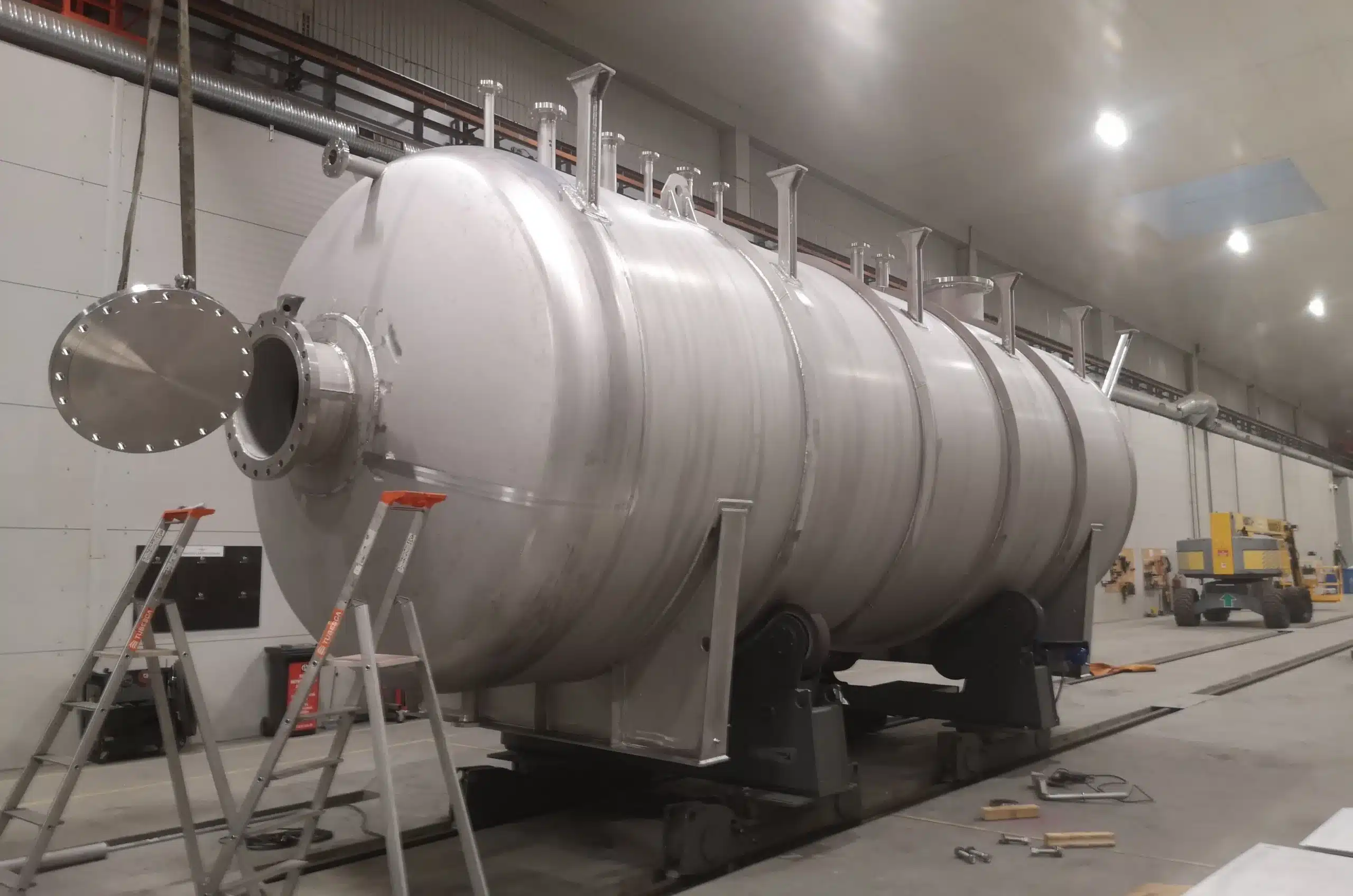 Stainless steel horizontal 57 m3 methanol storage tank rated for 7 barg being assembled by Western Technological Solutions in a modern workshop in Klaipeda, with the manhole, support frames, and fabrication tools visible around the pressure vessel.