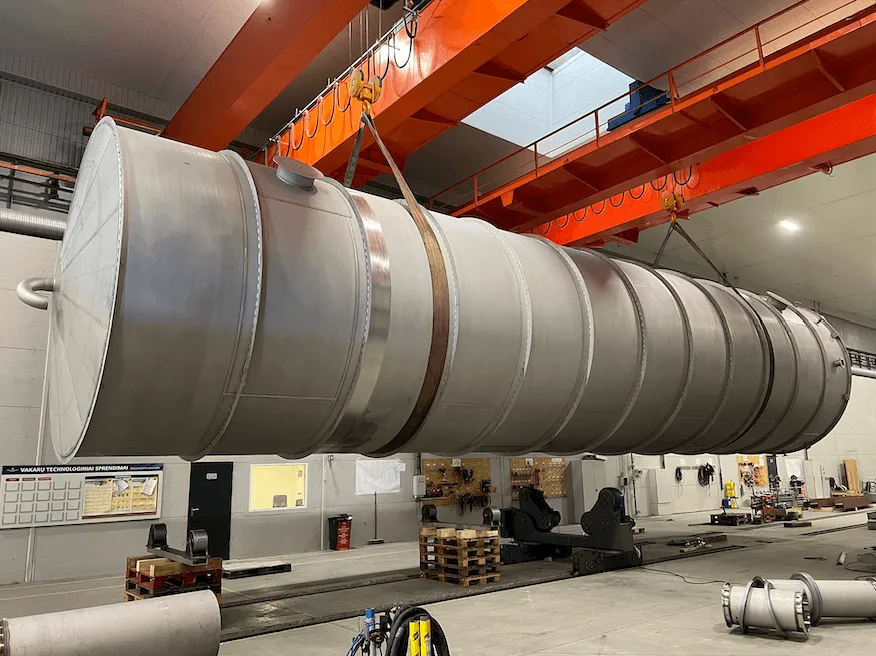 Large atmospheric stainless steel storage tank being lifted by a heavy-duty gantry crane during manufacturing inside the modern WTS fabrication workshop