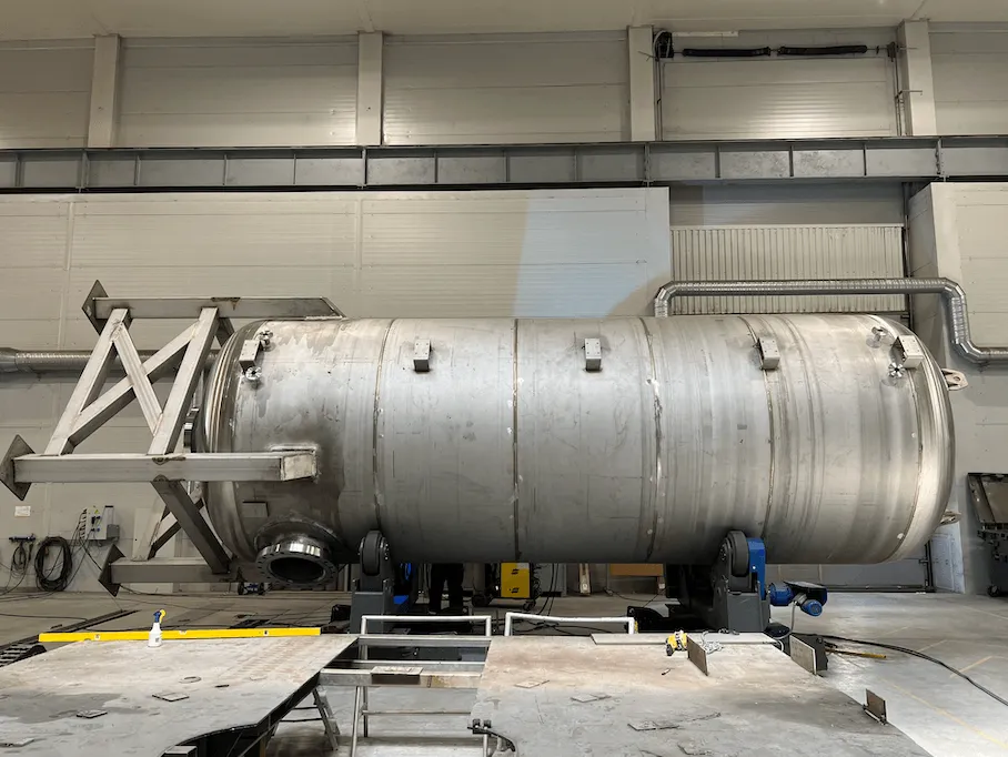 Large heavy stainless‑steel PED 2014/68/EU pressure vessel with reinforced supports positioned on turning rollers during fabrication in the Western Technological Solutions workshop in Klaipeda